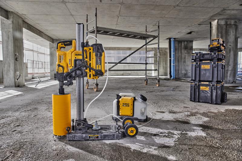 A DEWALT core drilling machine with a yellow cylindrical drill, water tank, and black storage boxes is set up on a concrete floor at a construction site.